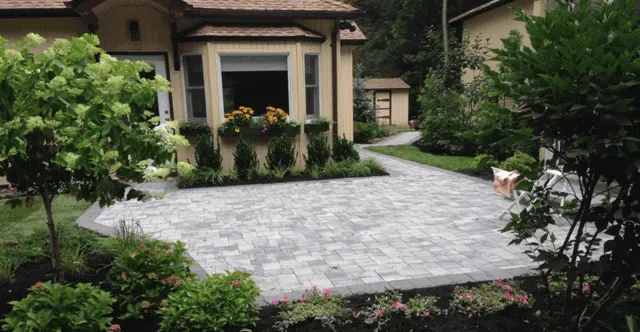 A brick driveway leading to a house surrounded by trees and bushes