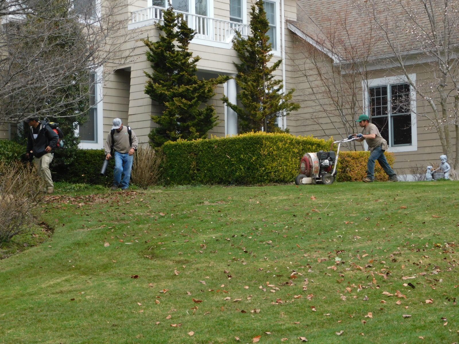 Three men are mowing a lush green lawn in front of a house