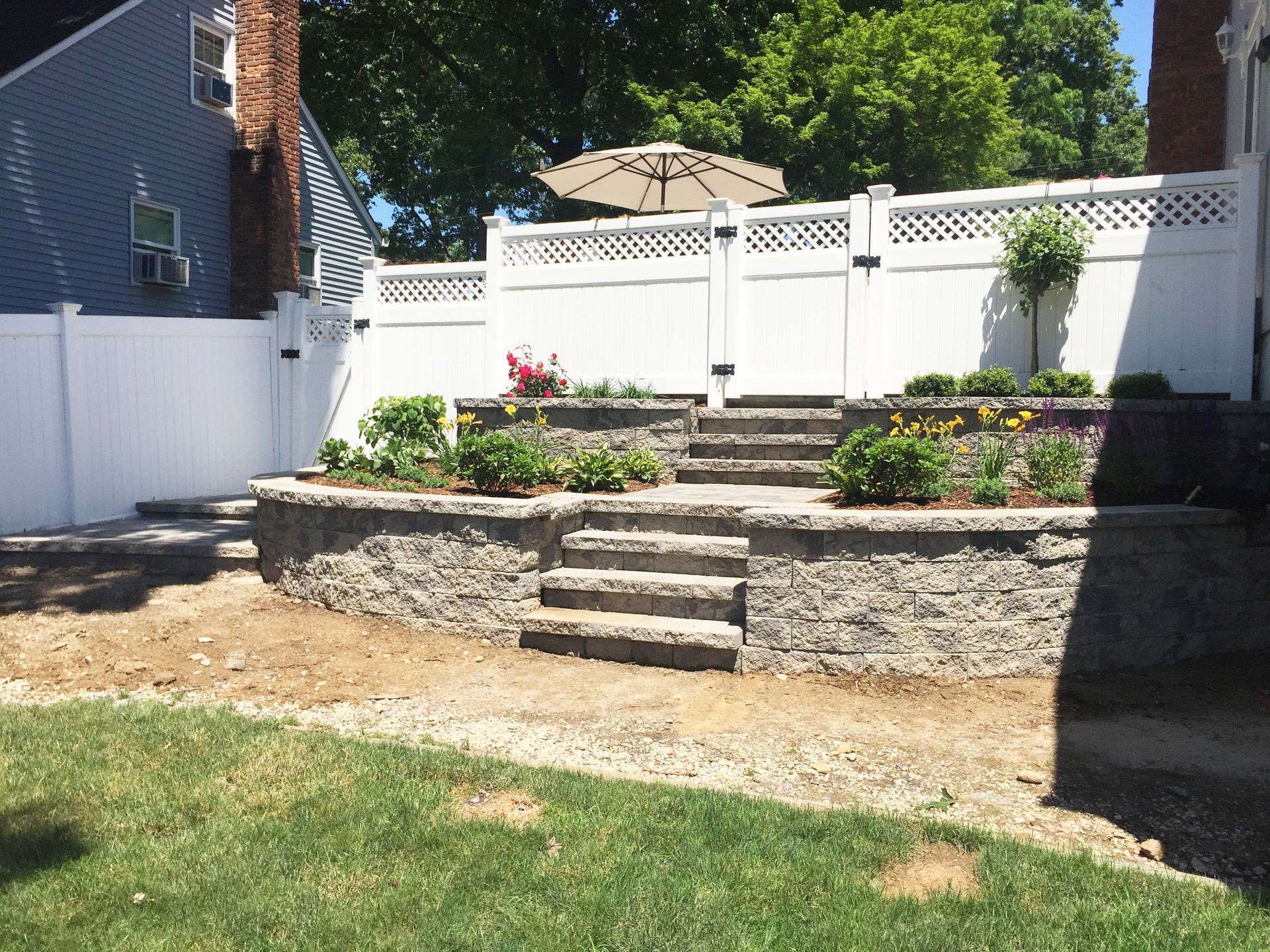 A backyard with a white fence and stairs leading up to a patio