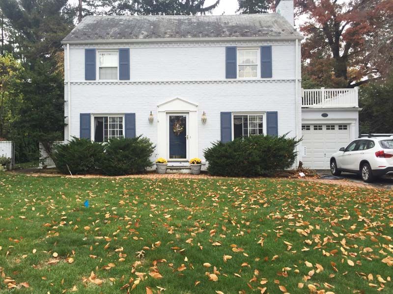 A white house with blue shutters and a white SUV parked in front of it