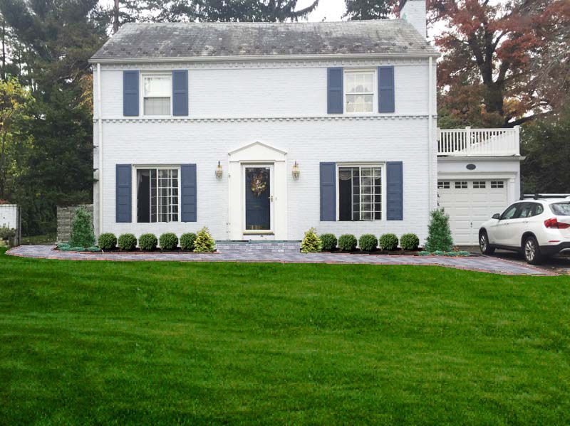 White house with blue shutters and a white SUV parked in front of it