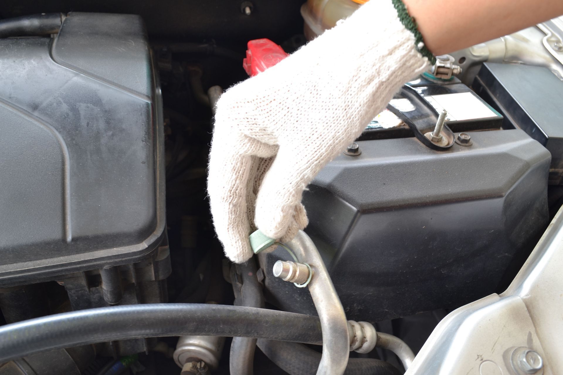 Gloved hand holding a car battery cable near an engine compartment