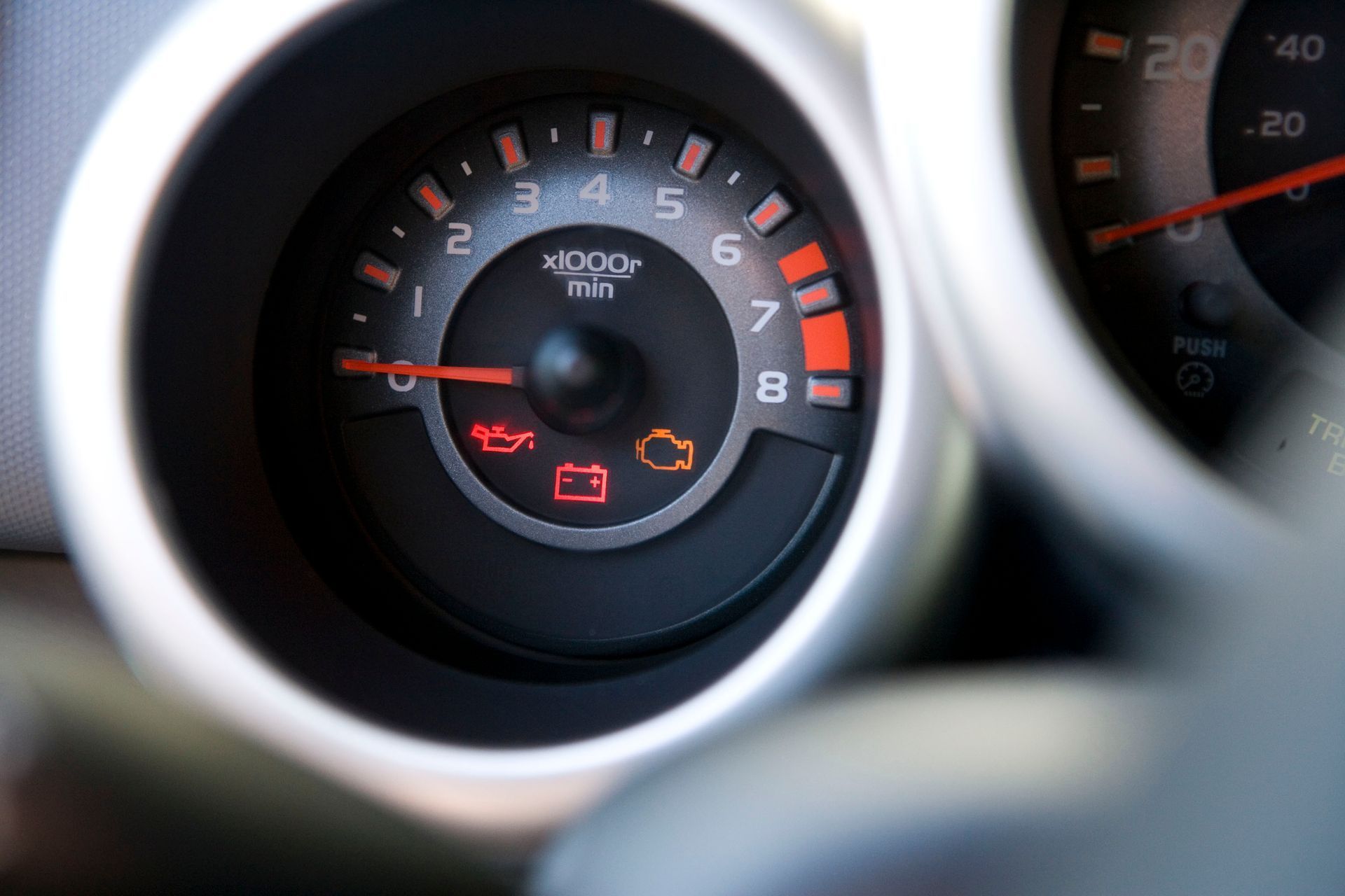 Close-up of a car dashboard tachometer and warning lights with a red needle and silver trim
