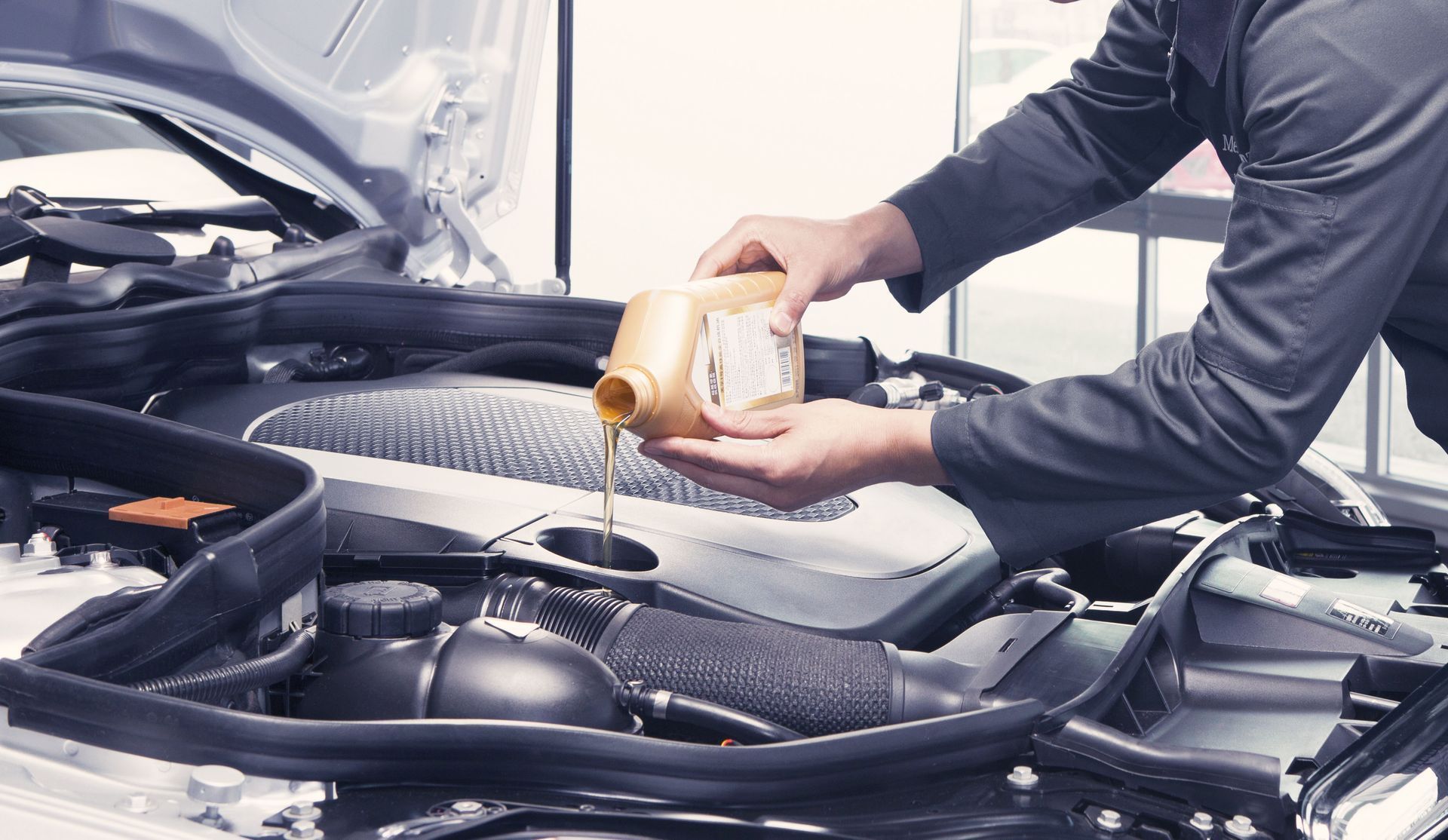 Person pouring motor oil into a car engine under the hood