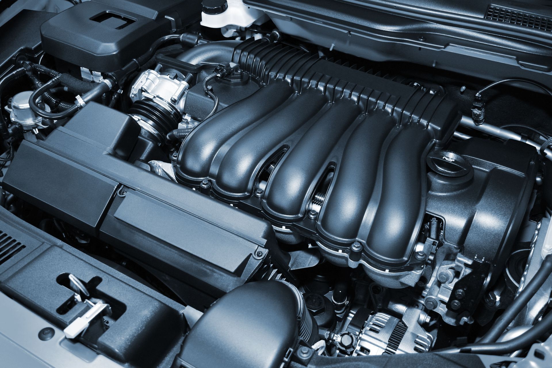 Close-up of a car engine with black plastic intake manifold and metal components under the hood