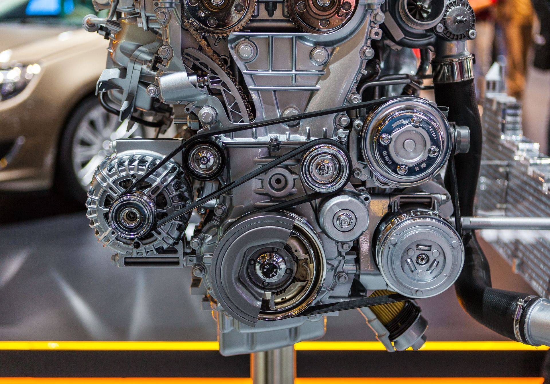 Close-up of a car engine with exposed belts, pulleys, and metallic components at an auto show display