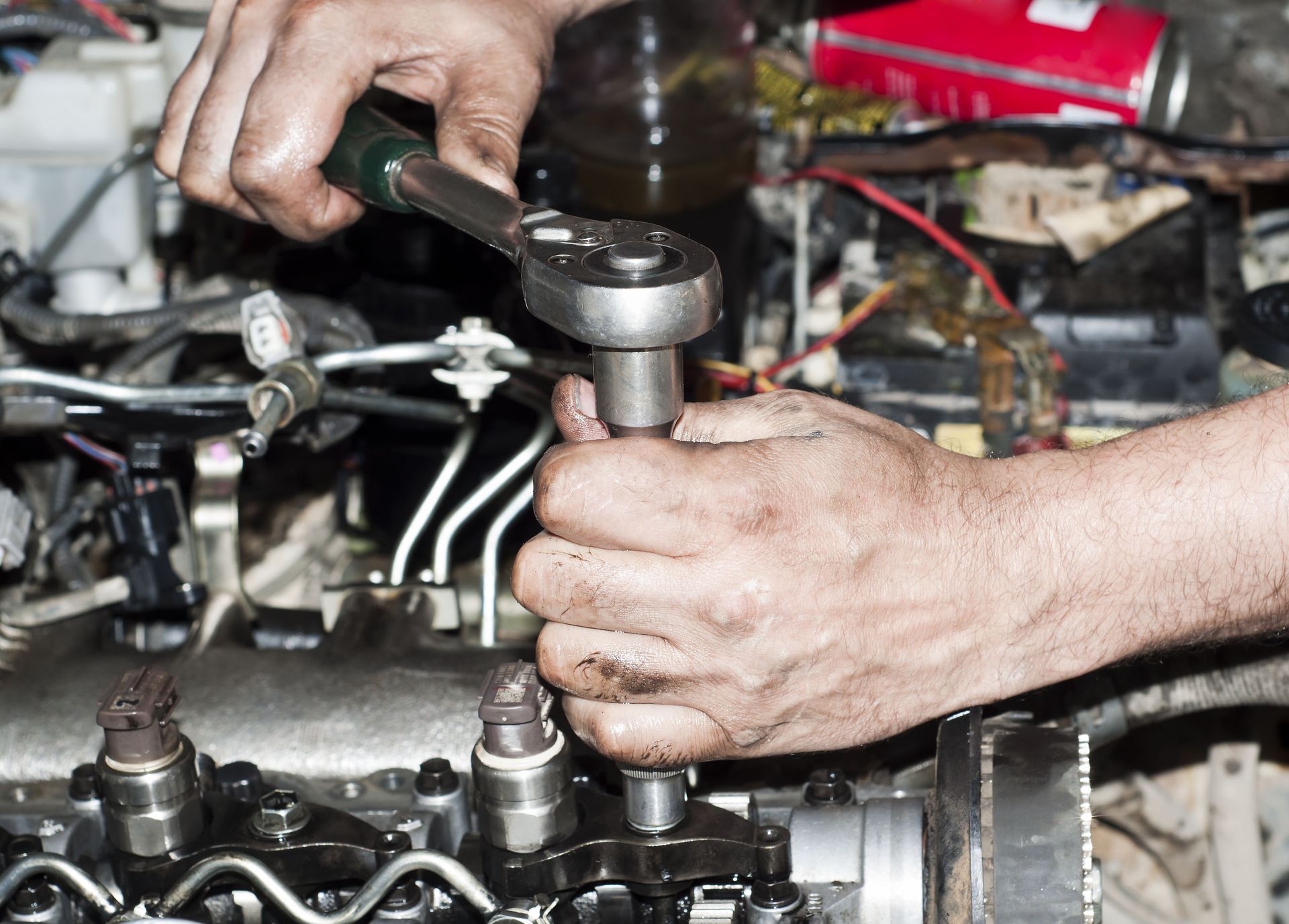 Hands using a wrench on an engine in a cluttered auto repair workshop