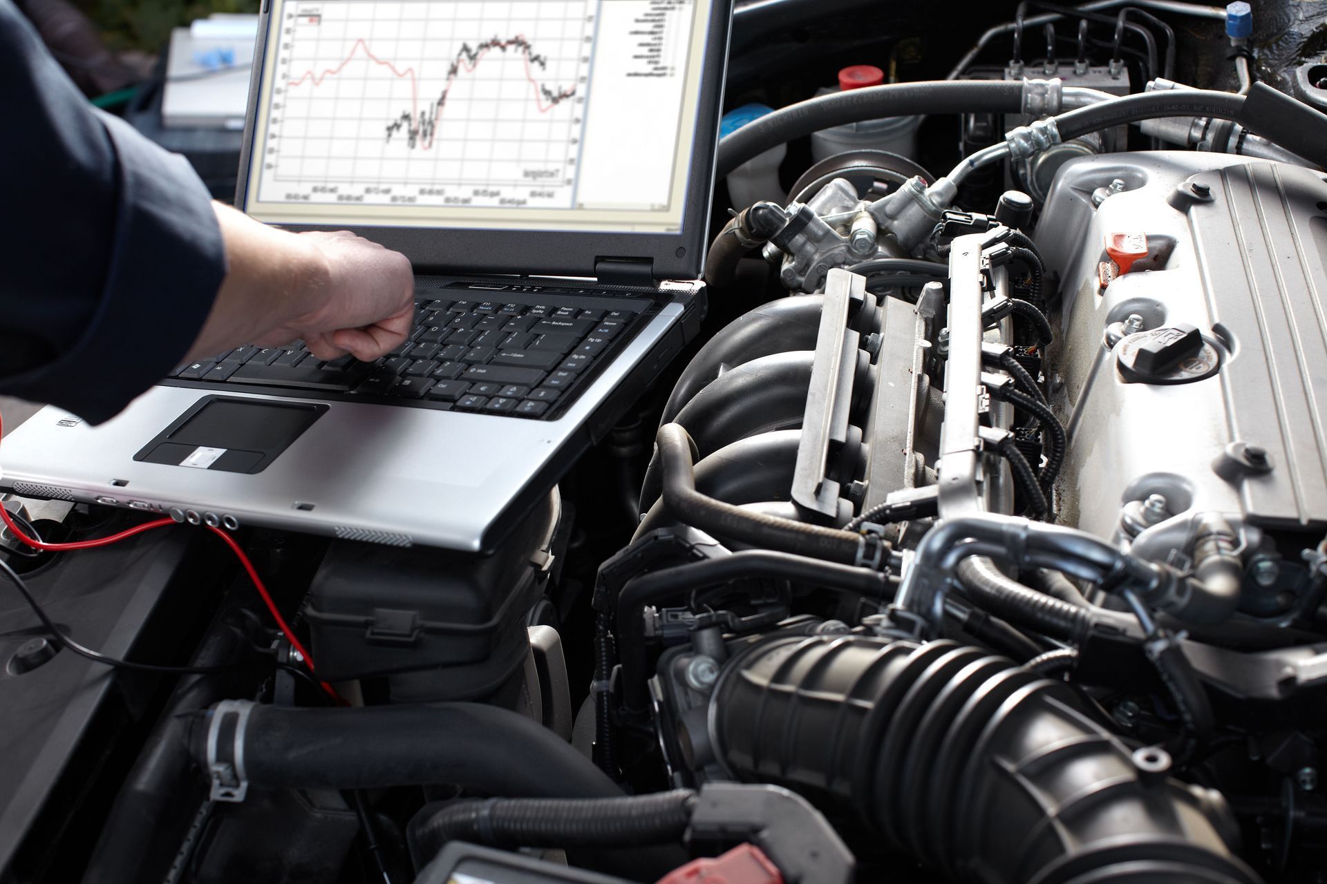 Mechanic using a laptop to diagnose a car engine in a garage