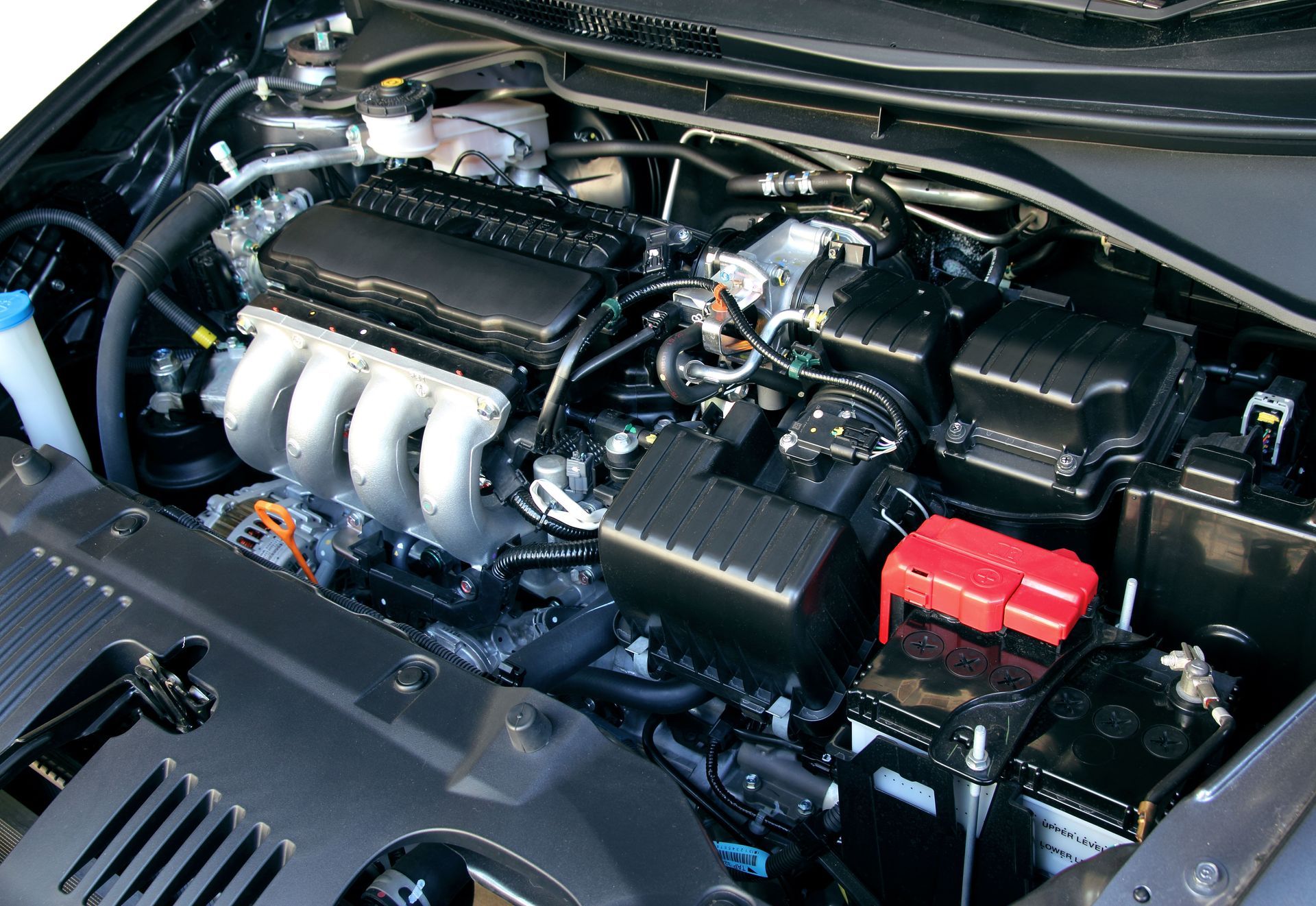 Car engine bay with silver intake manifold and black components, red battery cover on the right