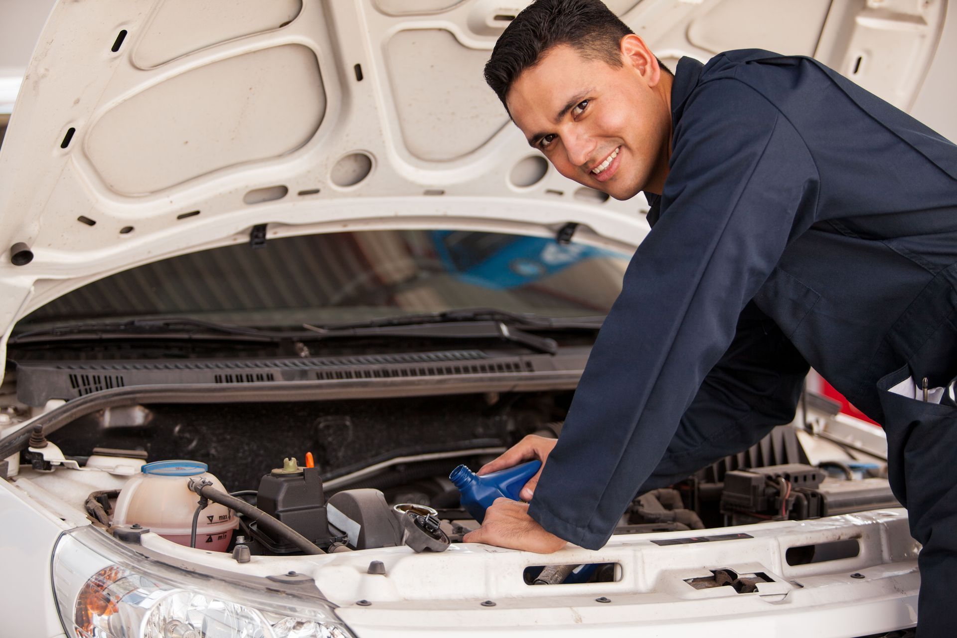 Mechanic in a dark shirt working under an open car hood in a garage