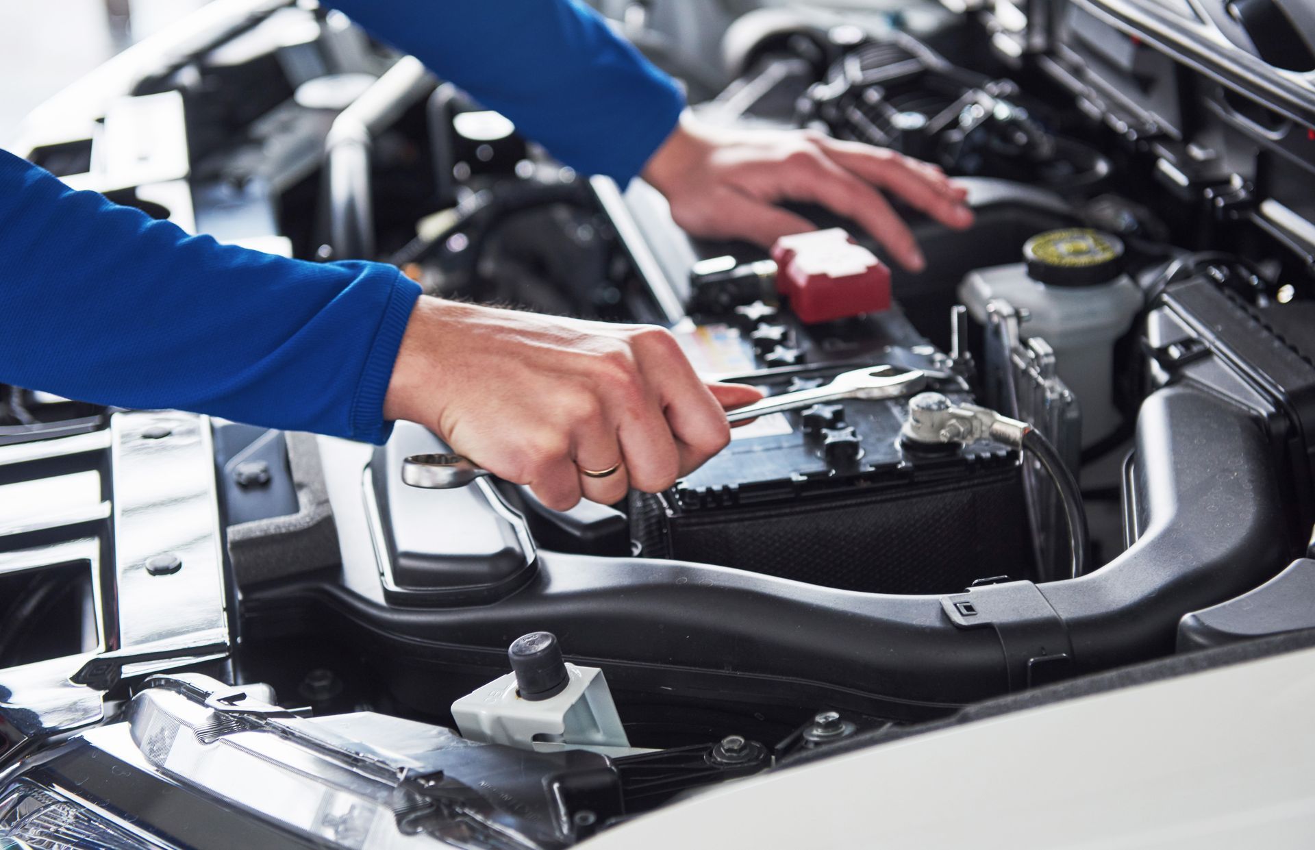 Mechanic working under a car hood with tools in an auto repair shop