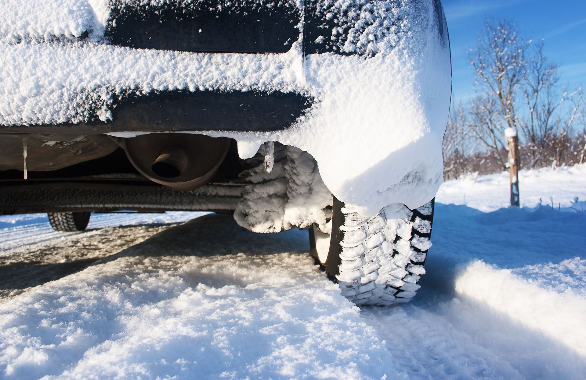 Snow-covered car tire and undercarriage in a snowy roadside scene