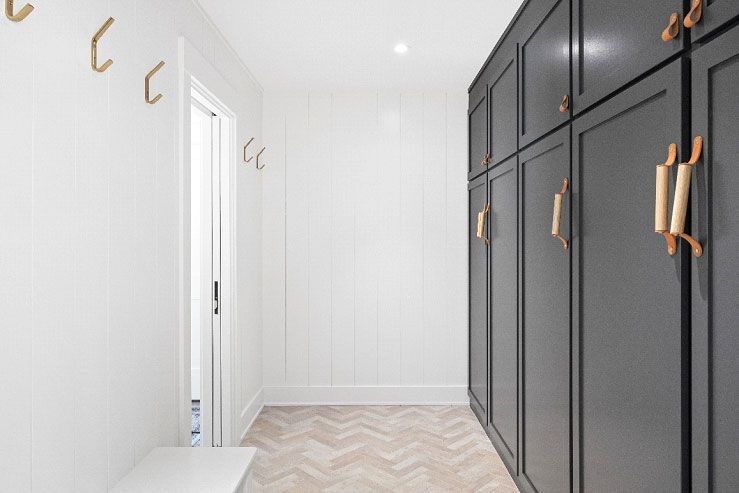 A hallway with black cabinets and gold handles and hooks on the wall