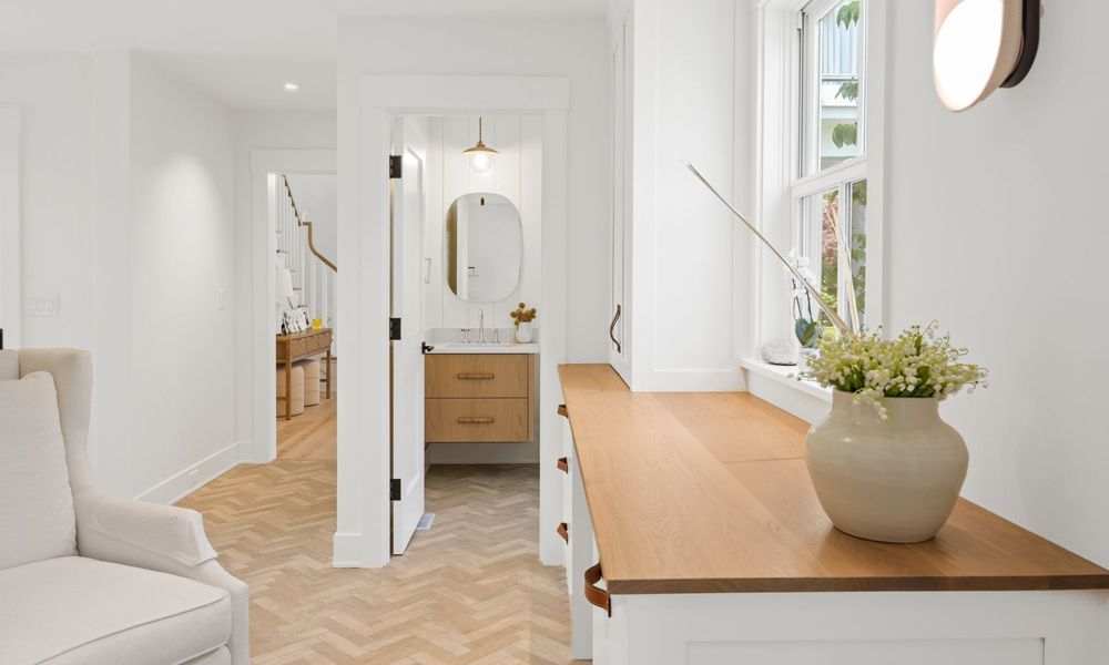 A wooden desk with a vase of flowers on it in a room with a chair.