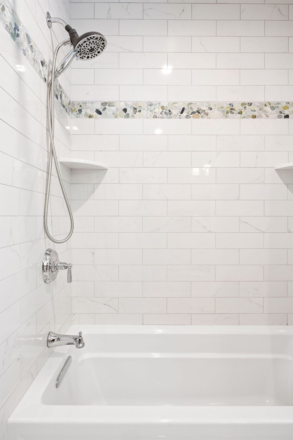 A bathroom with white tiles, a bathtub, and a shower head.