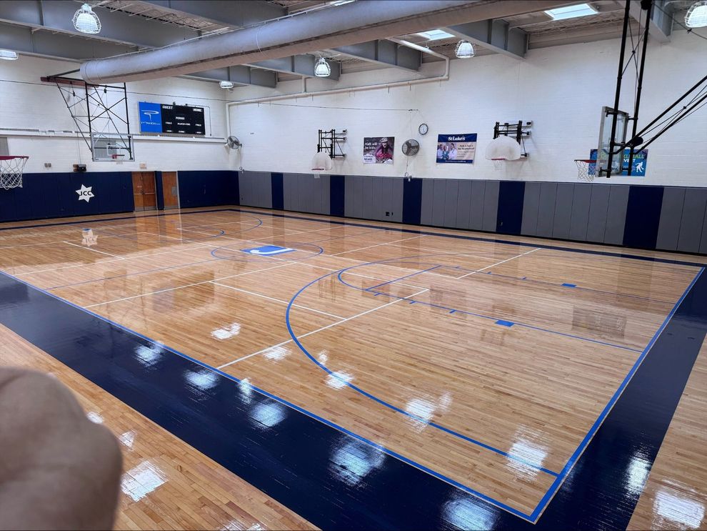 Indoor basketball court with polished wood floor, blue boundary padding, and overhead lights