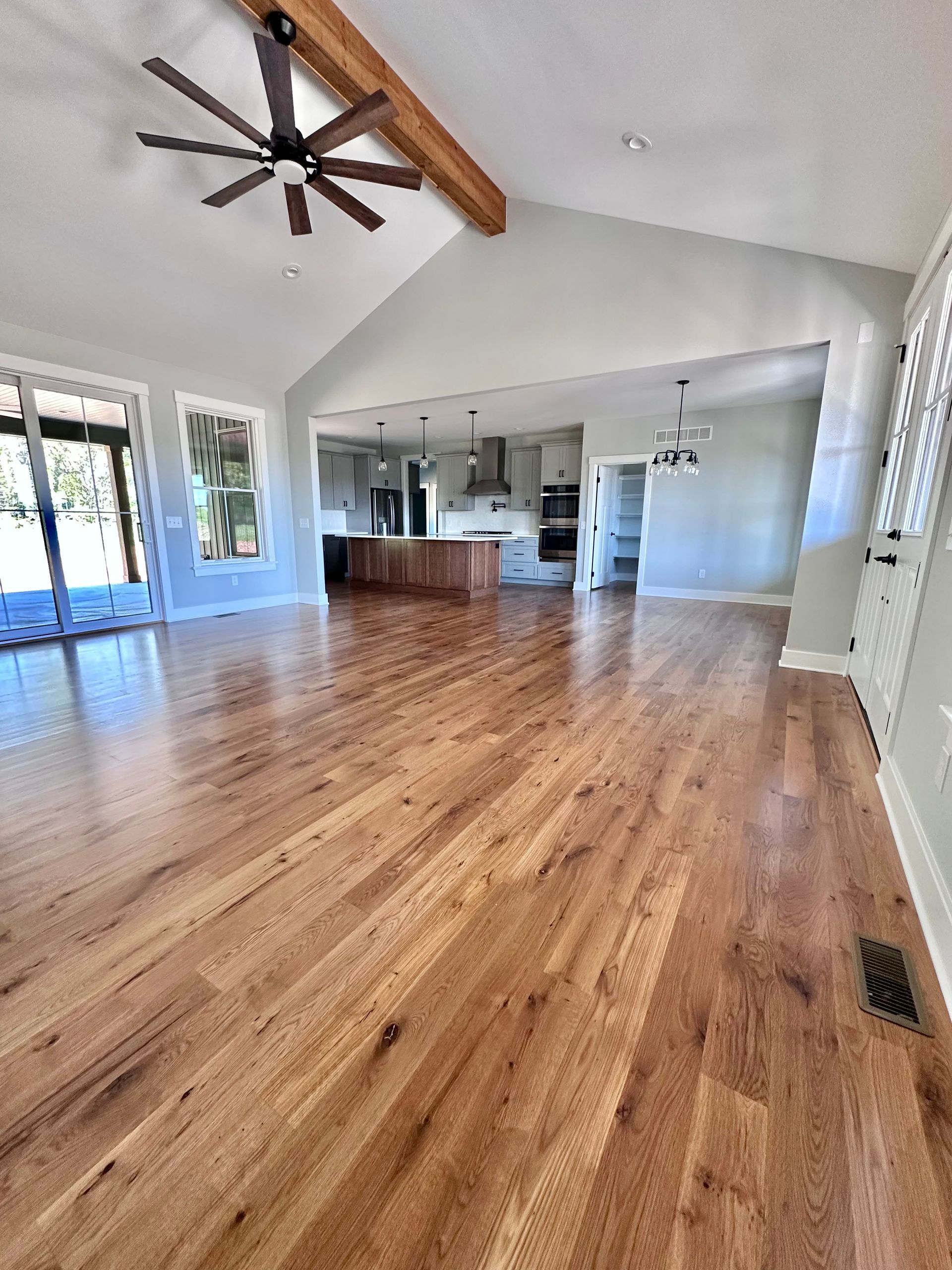 Bright open living room with hardwood floors, vaulted ceiling, ceiling fan, and a view into the kitchen.