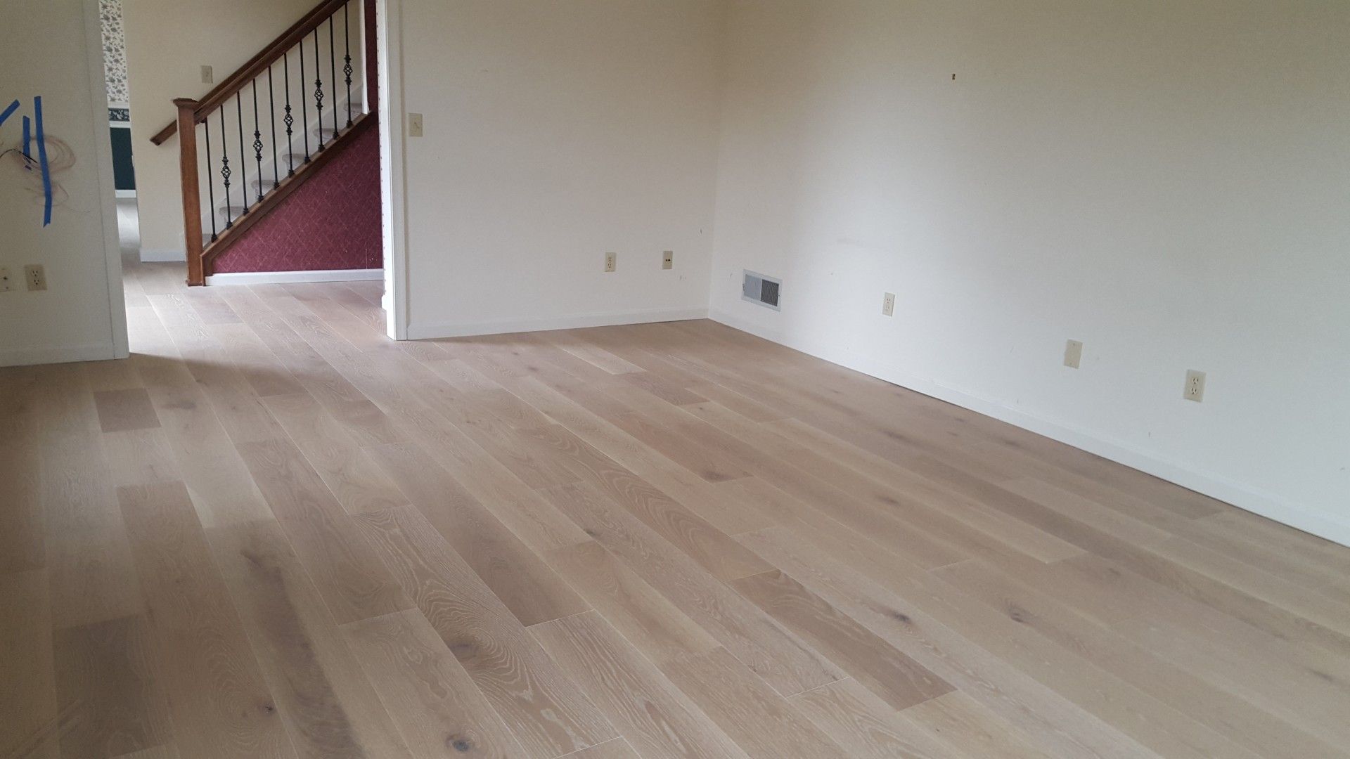 Empty room with light wood floors, white walls, and a staircase in the background