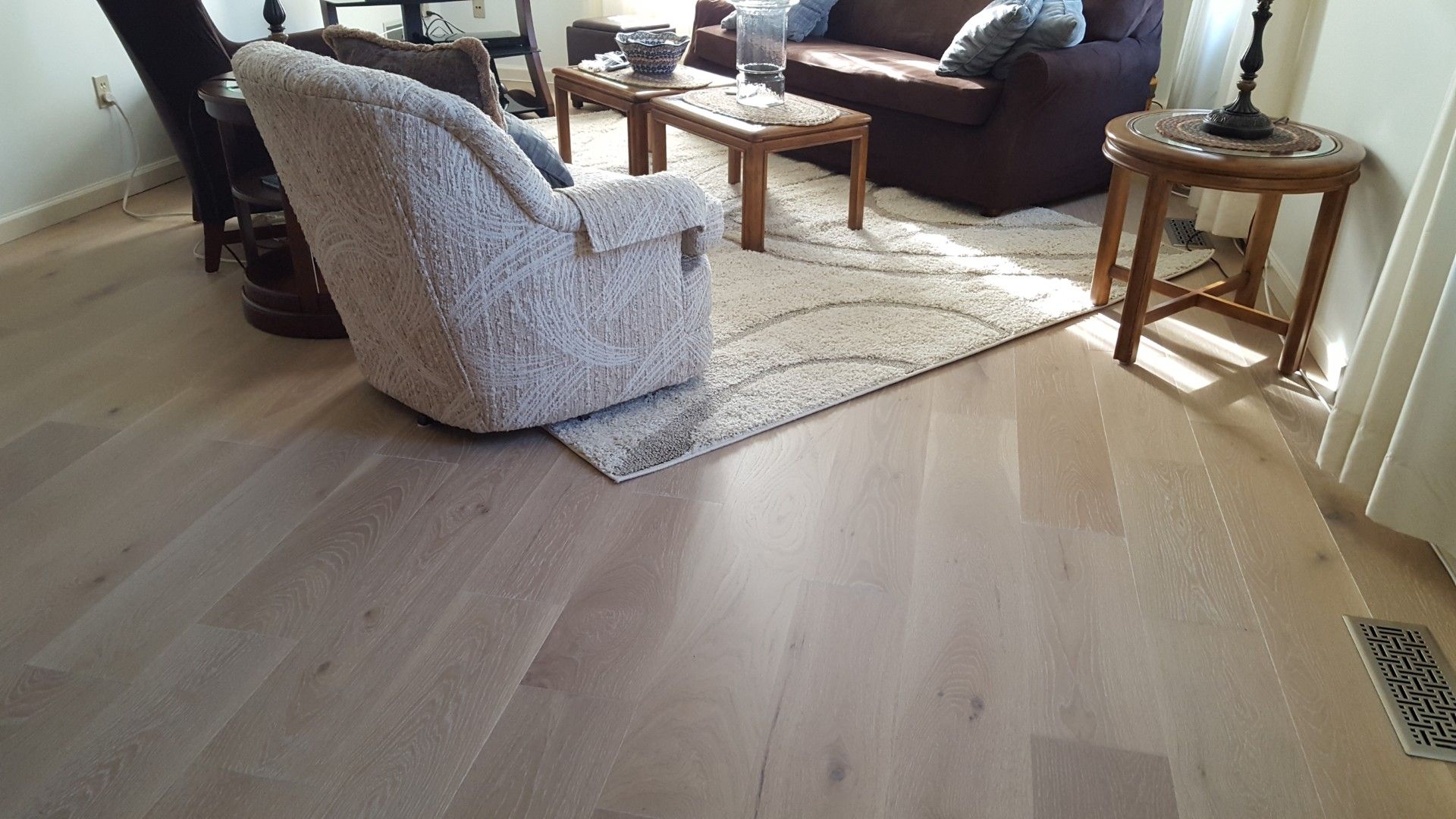 Living room with light wood floors, armchair, sofa, coffee table, and sunlight by the window