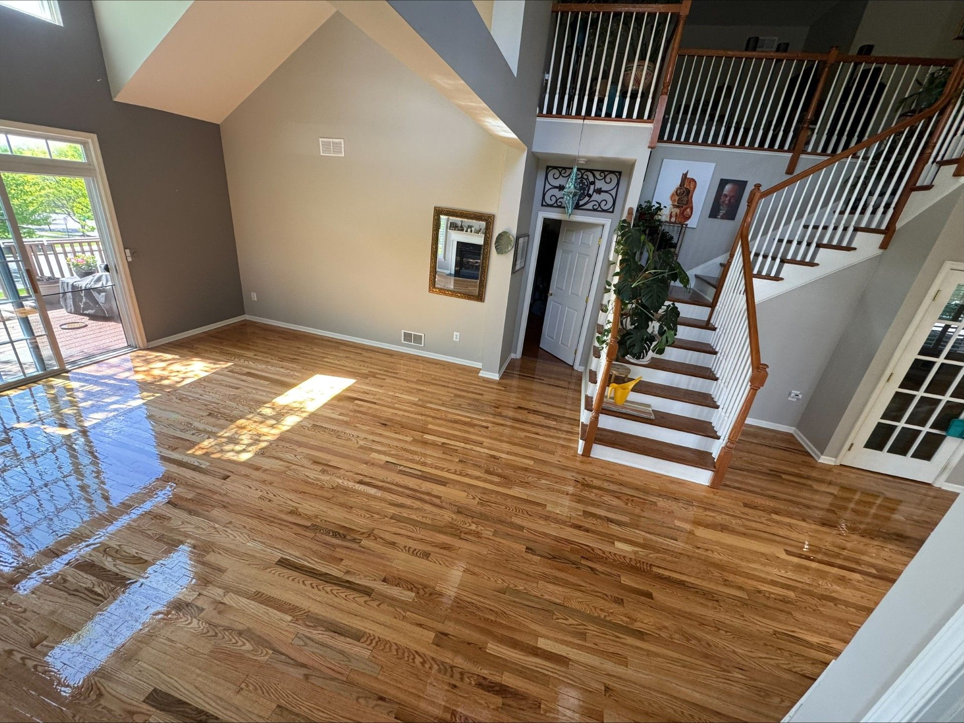 Bright empty living room with hardwood floors, tall windows, staircase, and vaulted ceiling