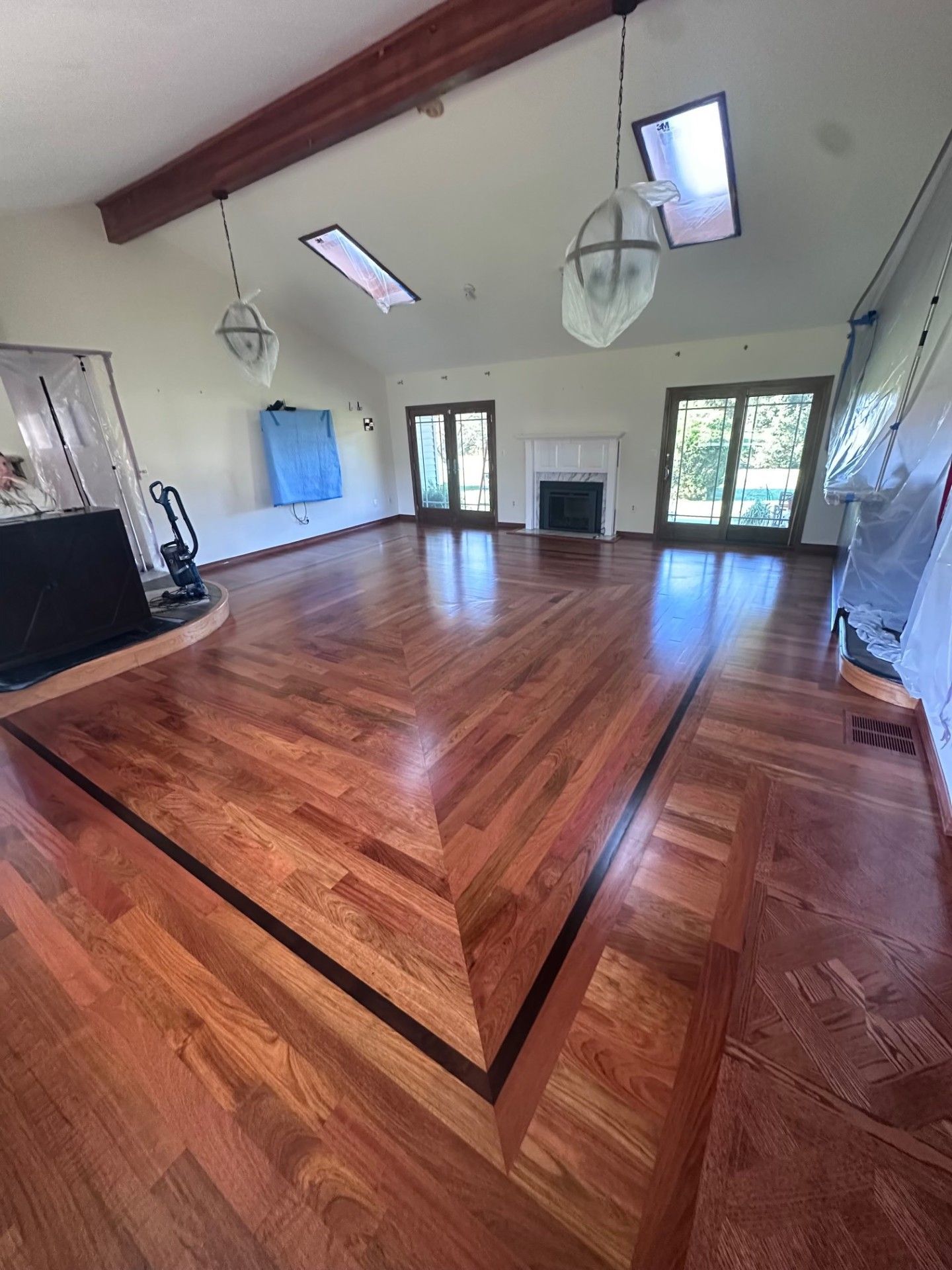 Empty room with polished wood floor, white walls, high ceiling, skylights, and fireplace