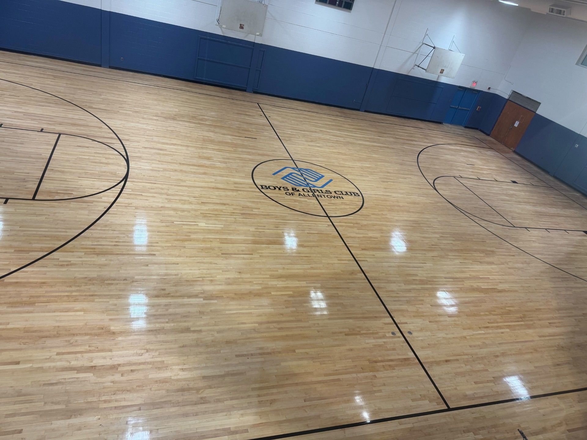 Empty indoor basketball court with a polished wood floor and blue-and-white walls.