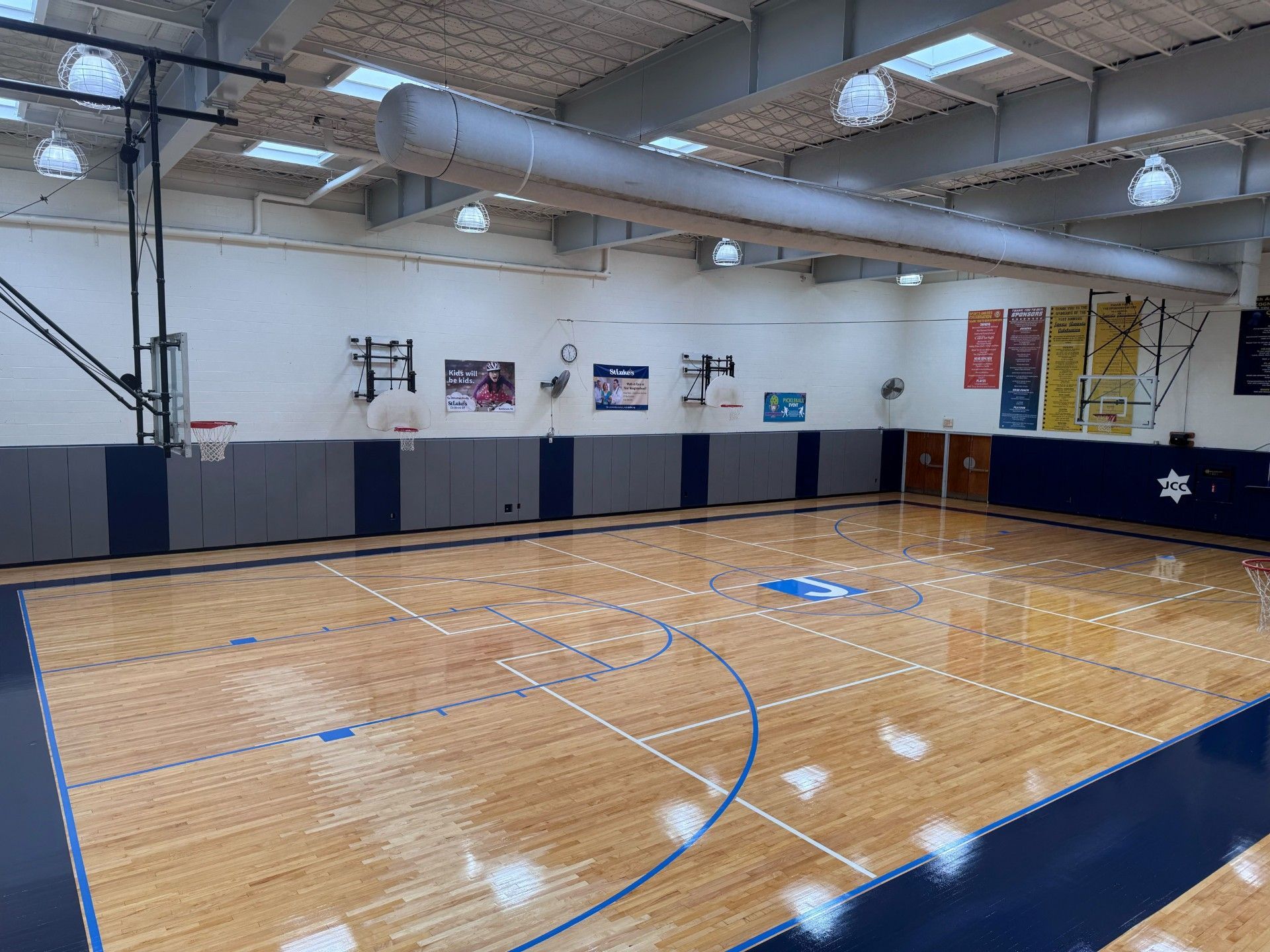 Empty indoor basketball court with polished wood floor, blue boundary lines, and wall banners under skylights
