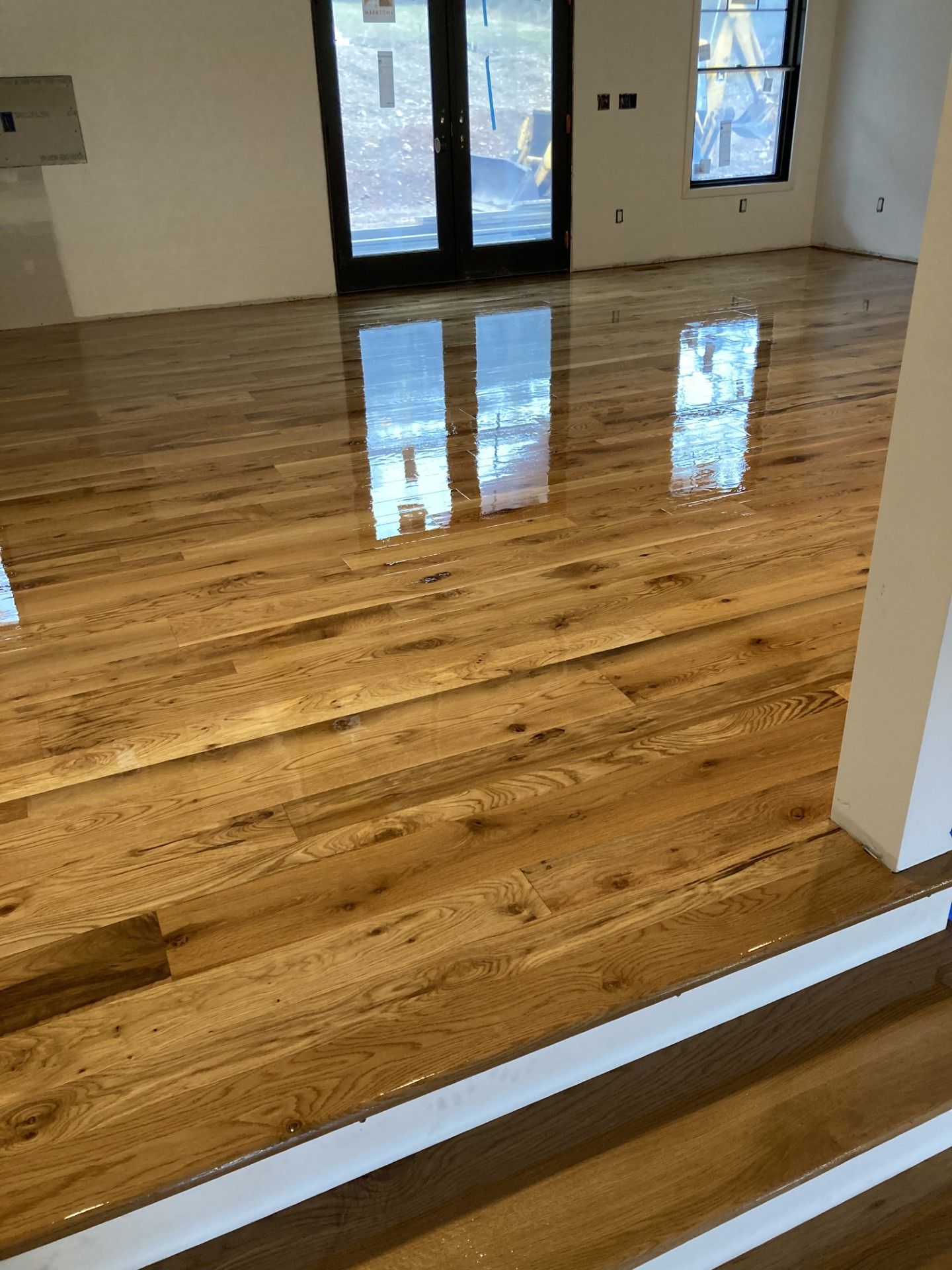 Polished, natural wood floorboards reflecting light in a room with a doorway and window.