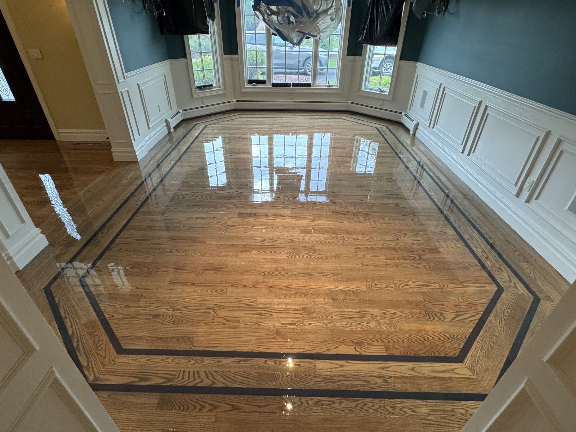 Polished hardwood flooring with dark wood inlay borders in a room featuring white wainscoting and blue-toned walls.