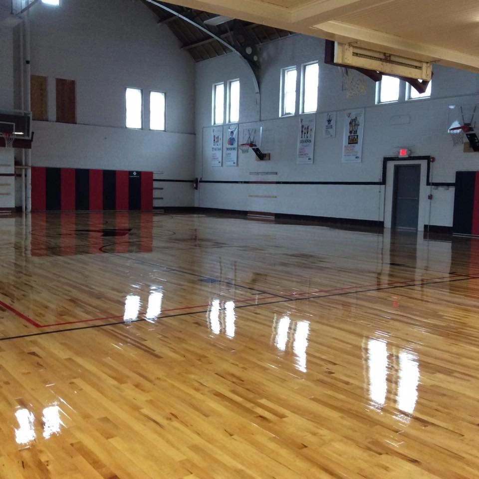Empty basketball court with shiny wooden floor, arched windows, and black and red padded walls.
