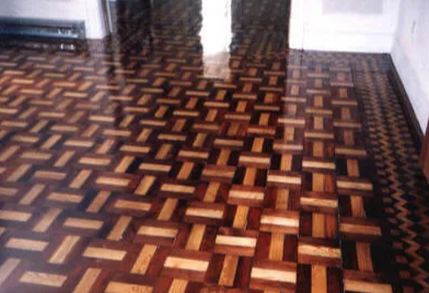 Close-up view of a shiny, patterned hardwood floor with alternating light and dark wooden blocks.