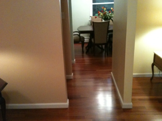 Hallway with wooden floor leading to a dining room with a table and chairs, light-colored walls.