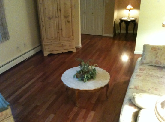 Wooden floor in living room with a table, cabinet, and couch.