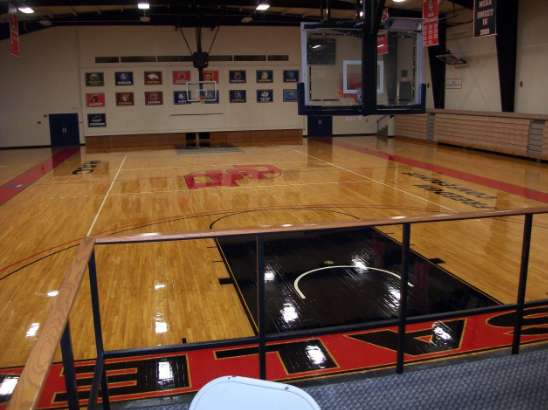 Basketball court, shiny wood floor, black and red accents, bleachers, banners on wall.