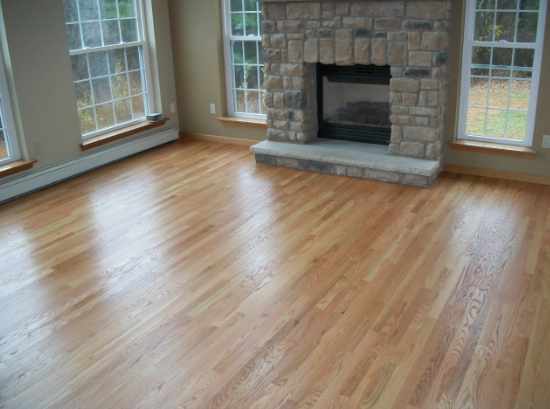 Hardwood floor in a living room, with windows and a stone fireplace.