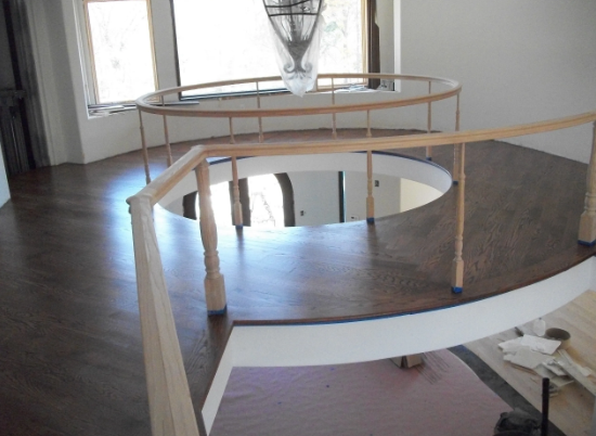 Circular hardwood floor with a railing overlooking a lower level, natural light.