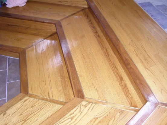Wooden floor with geometric patterns and dark brown trim, reflecting light.