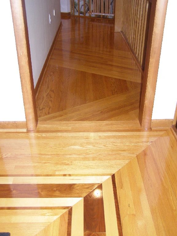 Wooden flooring with geometric patterns in a hallway with a doorway and stairs visible.