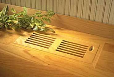 Wooden floor vent with rectangular slats, built into a light-colored wooden surface. Green plant stems are visible.