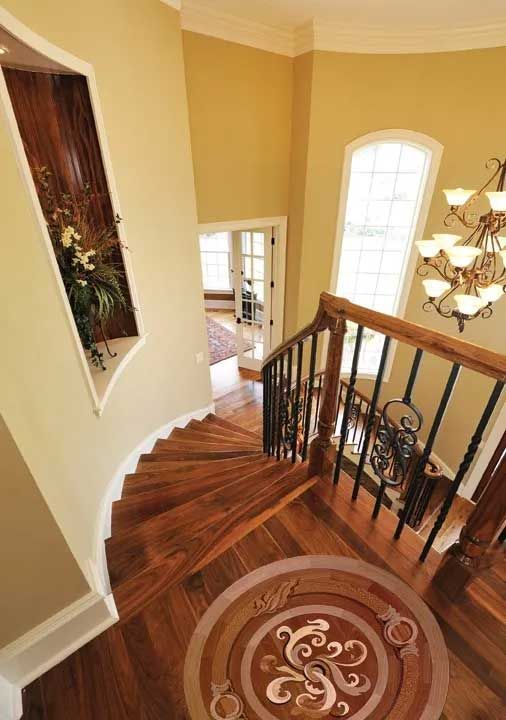 View down a curved staircase with decorative wooden flooring and a chandelier.