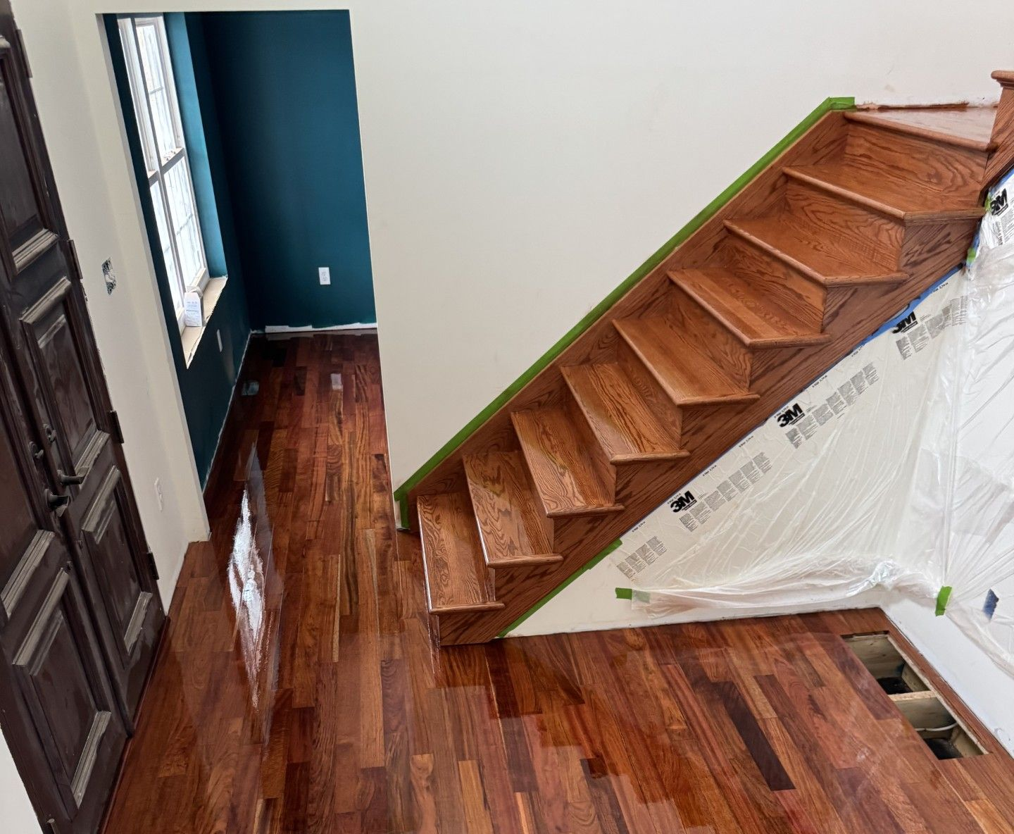 A high-angle view of a room with polished, dark wood plank flooring and a matching wooden staircase along a white wall.