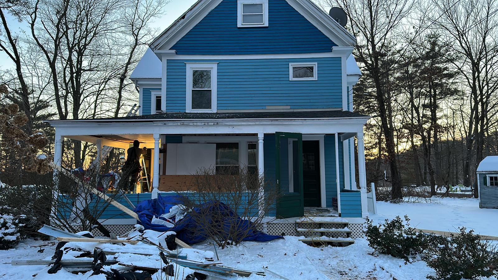 A blue house with a porch in the snow.
