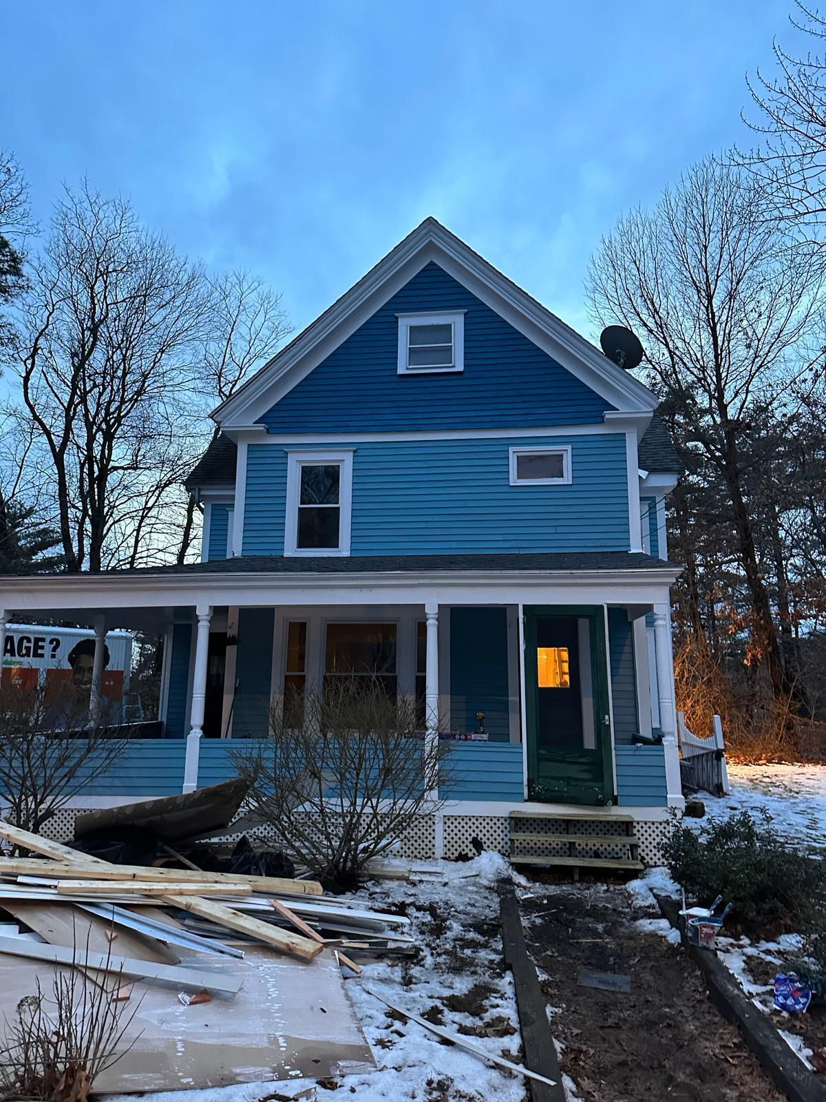 A blue house with a porch is being remodeled in the snow.