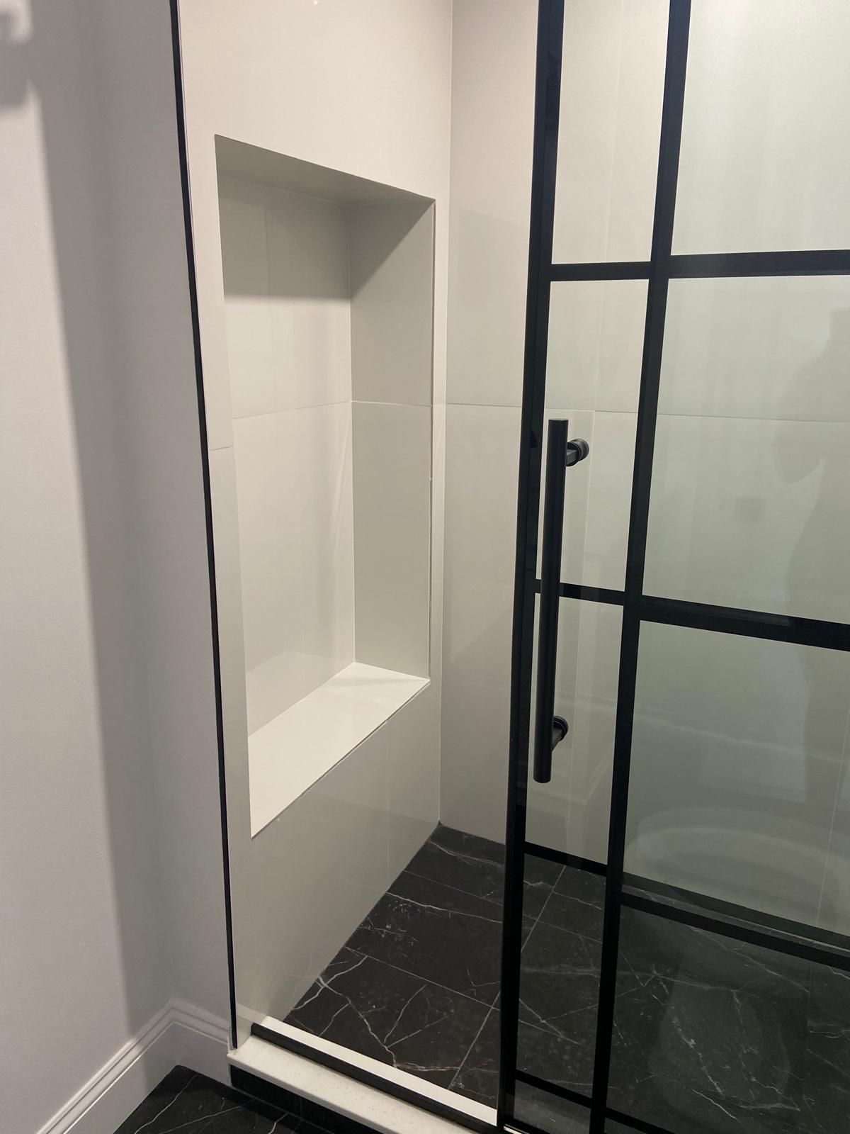 A bathroom with a black shower door and a niche in the wall.