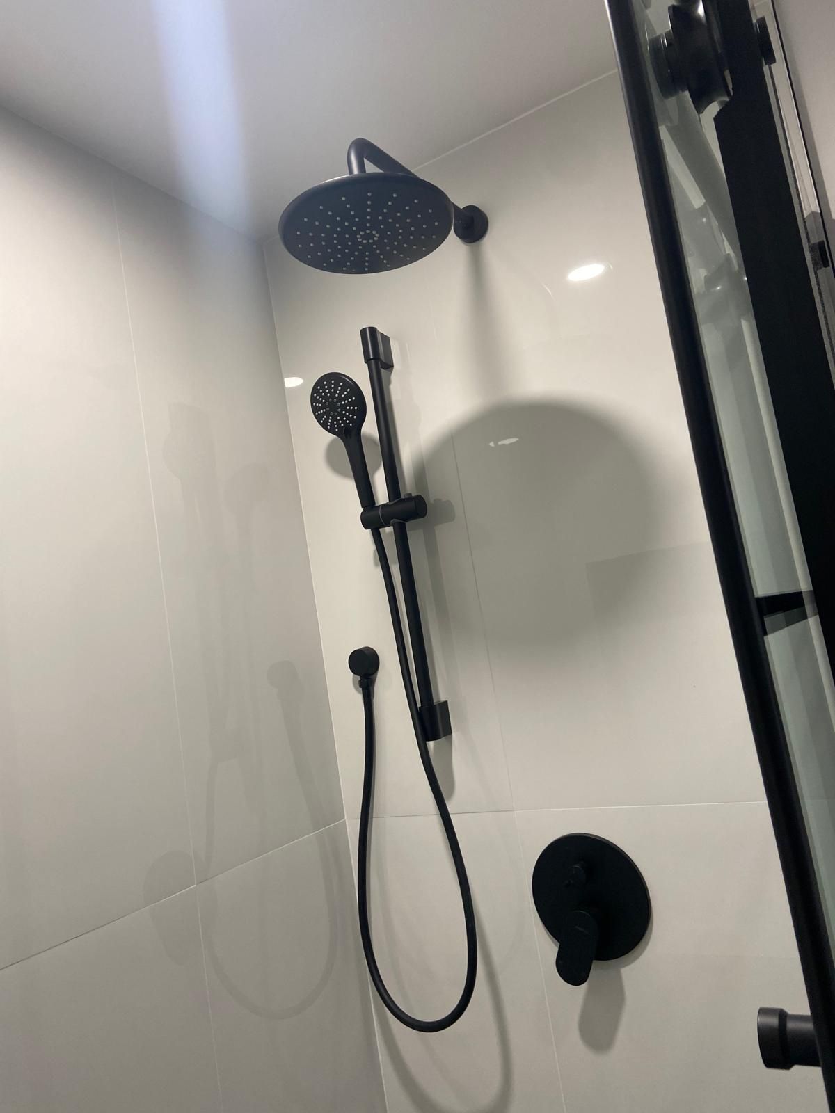 A black shower head is hanging from a white wall in a bathroom.