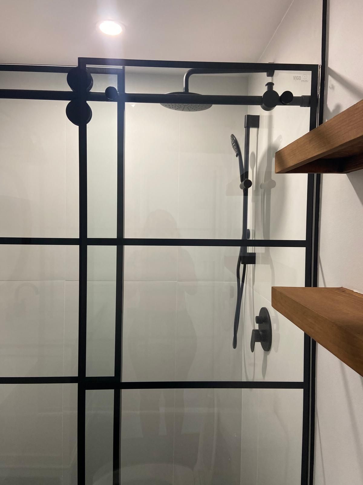 A bathroom with a sliding glass shower door and a wooden shelf.