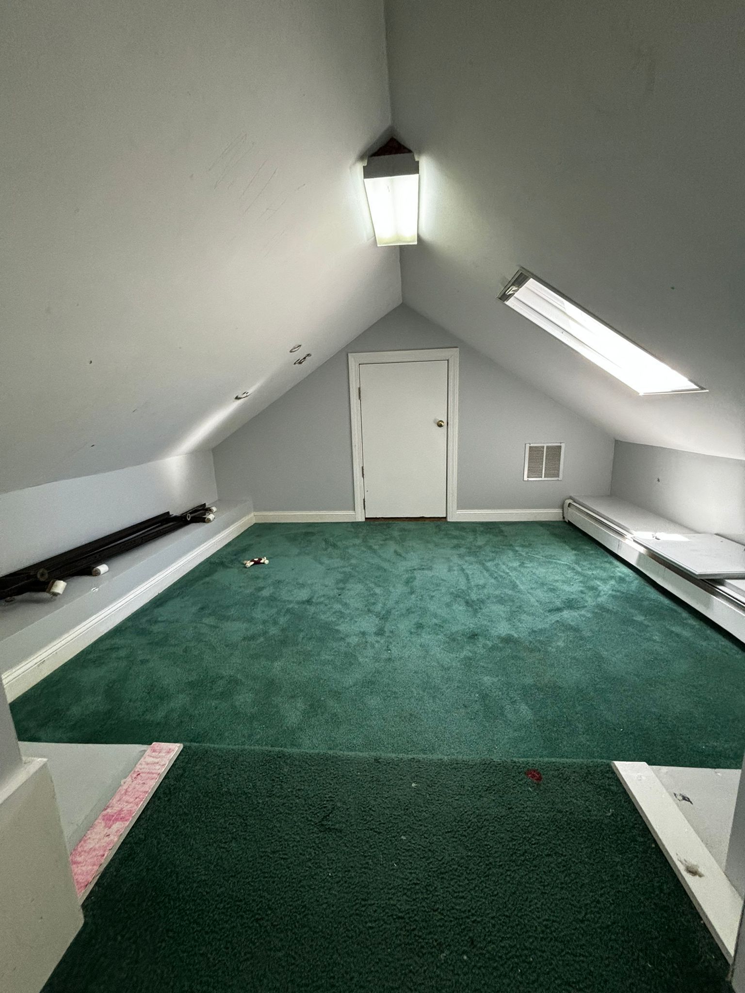An empty attic with a green carpet and a skylight.