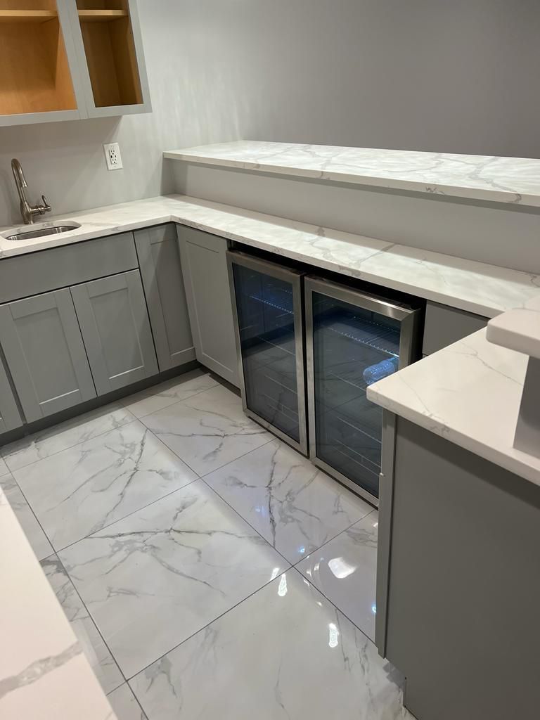 A kitchen with marble floors, gray cabinets, a sink, and a refrigerator.