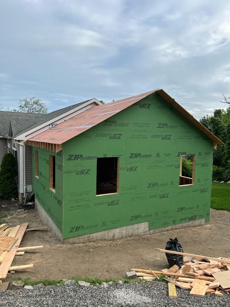 A small house is being built with green siding and a red roof.