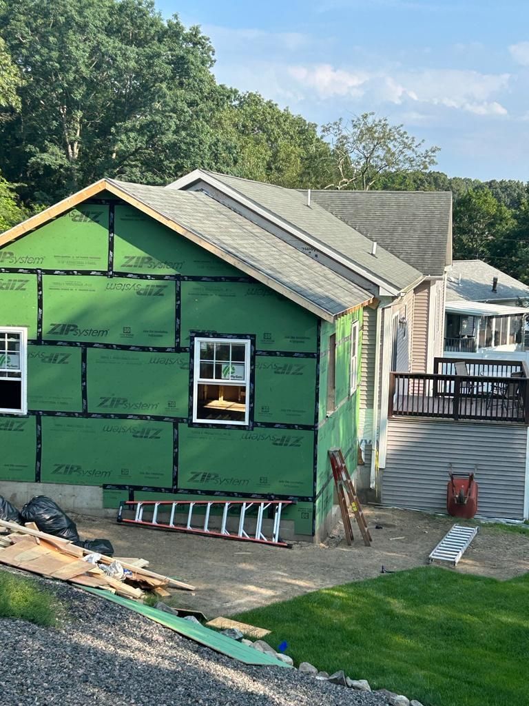 A house is being remodeled with green siding and a ladder in front of it.